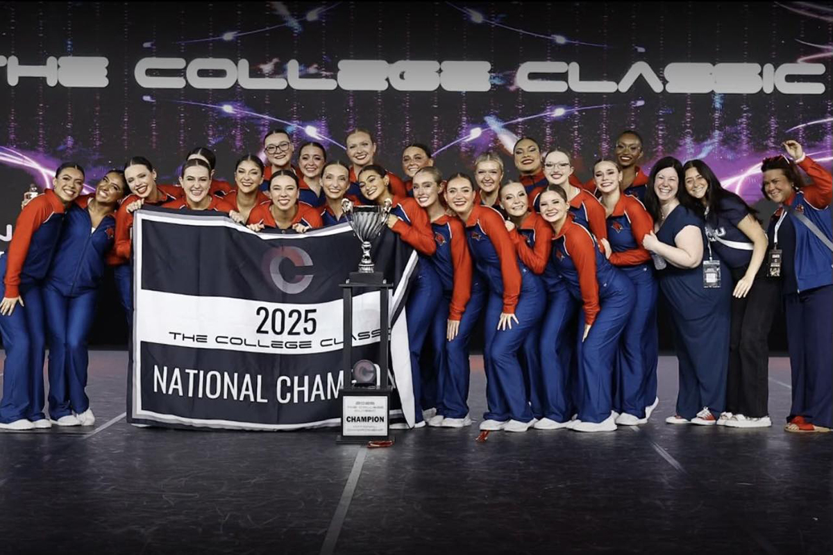 group of people in red and blue uniforms holding banner standing in front of large trophy